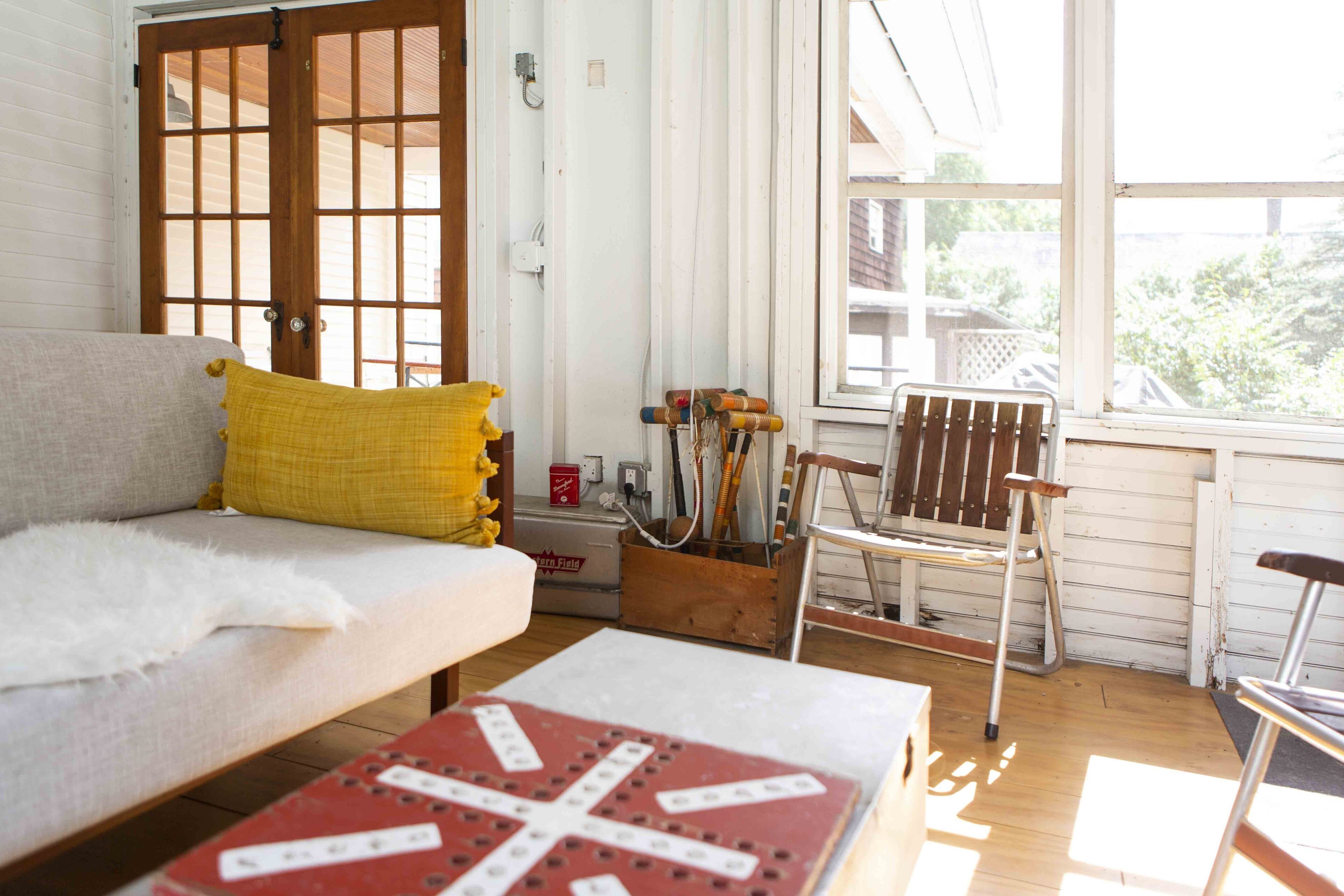 A cozy living room with a sofa, a wooden chair, and a red table with a cross design.