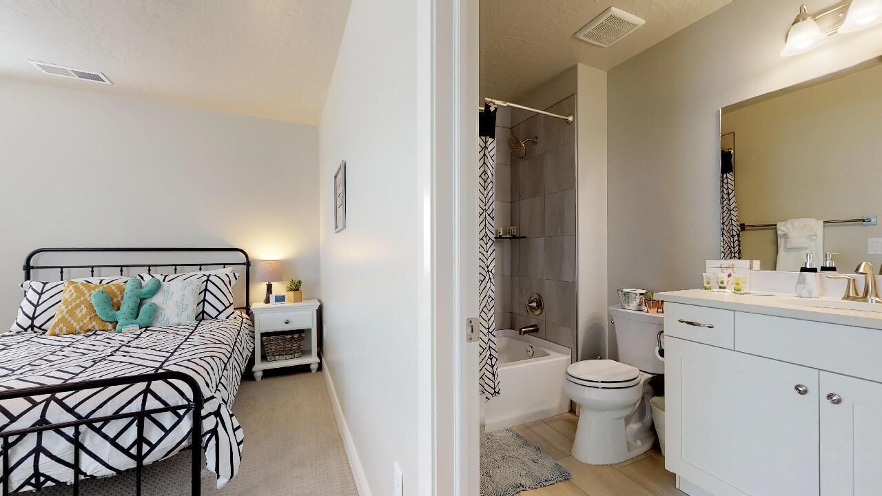 A bedroom with a bed, bedside table, and a bathroom with a bathtub, toilet, and sink.