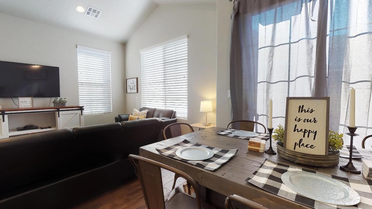 A dining area with a table set for two, a sofa, and a television in the background.