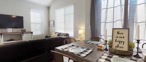 A dining area with a table set for two, a sofa, and a television in the background.