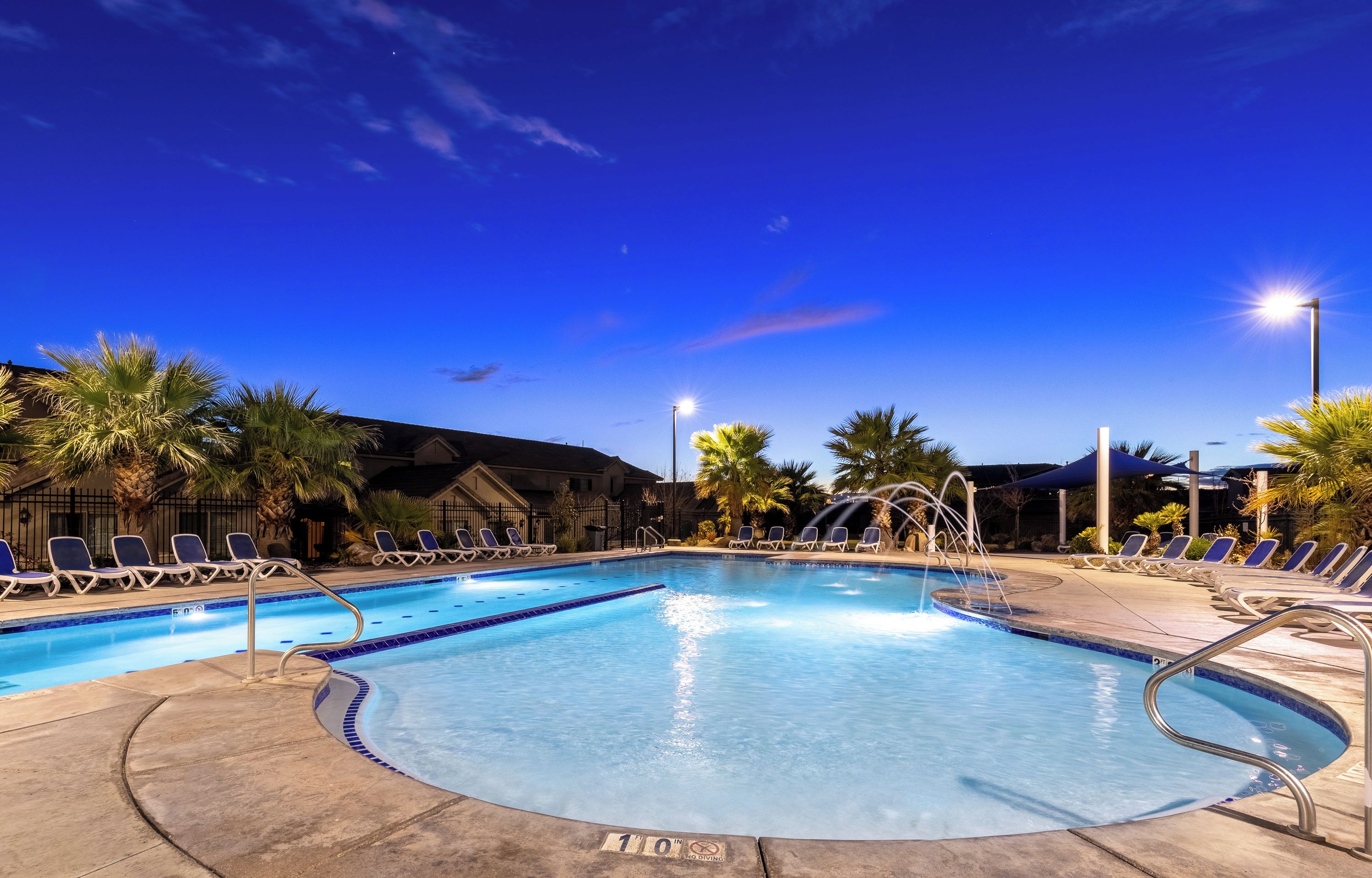 A swimming pool with lounge chairs and palm trees, surrounded by buildings.