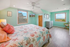 A bedroom with a bed, a ceiling fan, a dresser, and a view of the beach. - Oceanfront Dog Friendly Home with Easy Beach Access, Grill, and Smart TVs (Avon)
