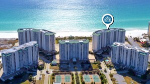 A high-rise hotel complex with multiple buildings, a central courtyard with tennis courts, and a beachfront view.