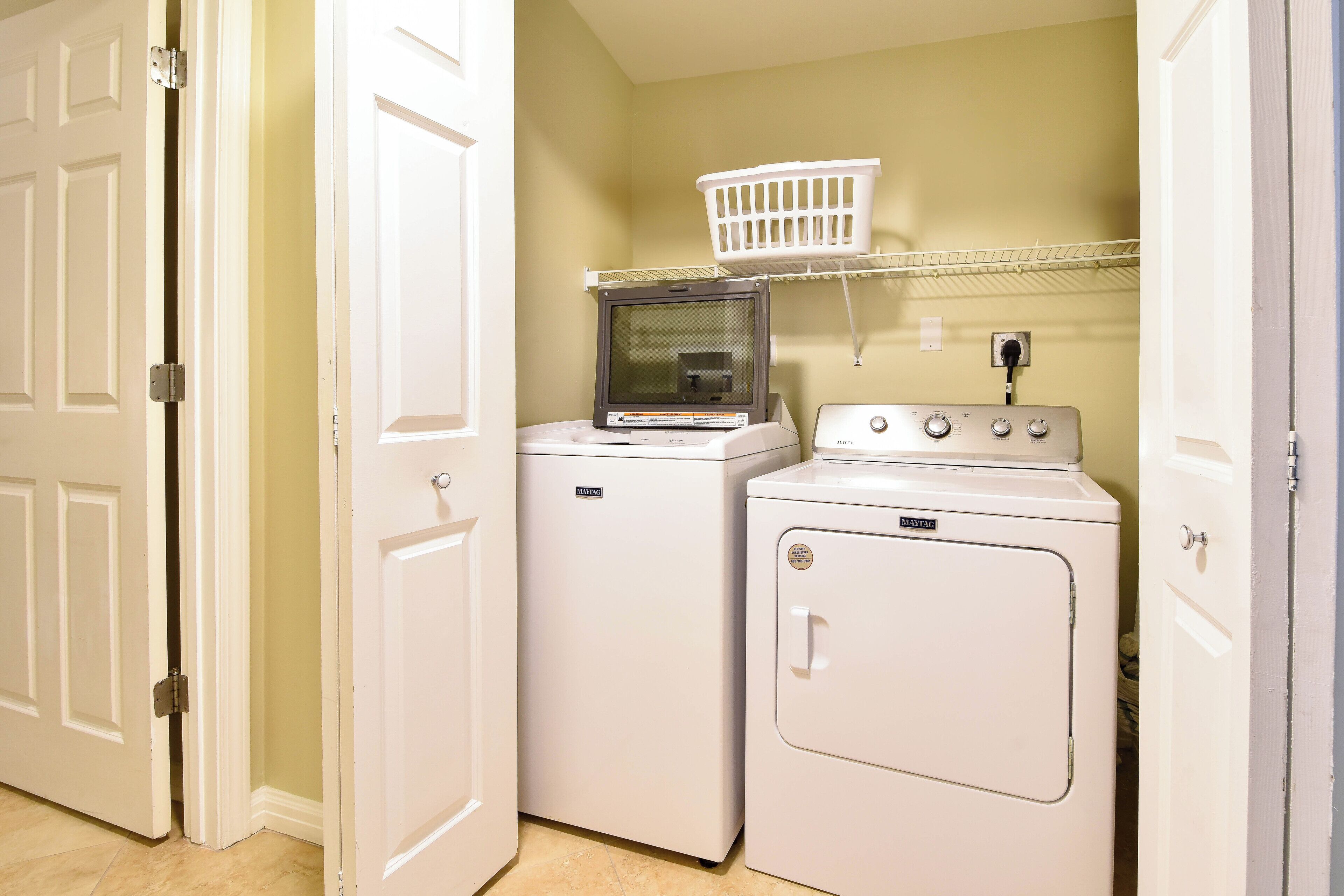 A laundry room with two white washing machines, a dryer, and a white laundry basket on a shelf.