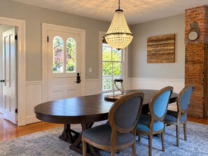 Un coin repas avec une table ronde, des chaises, un lustre et une vue par la fenêtre.