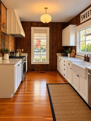 Une cuisine avec un lambris en bois, des meubles blancs, une fenêtre centrale et un luminaire suspendu.