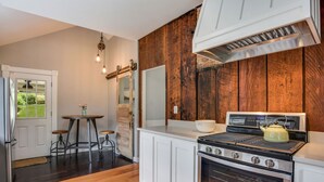 Une cuisine avec un mur en bois, des placards blancs, une cuisinière et un évier.