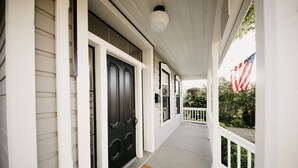 Un porche avec une porte noire, des balustrades blanches et un drapeau américain.