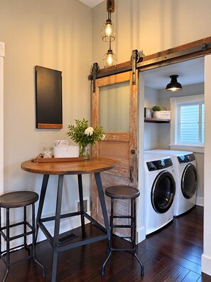 Une buanderie équipée d’un lave-linge, d’une table en bois avec des tabourets et d’un luminaire suspendu.