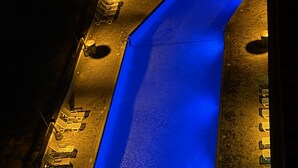 Vue aérienne d ’une piscine dont l’intérieur est illuminé de lumière bleue, entourée de chaises longues et d’un mur en briques.