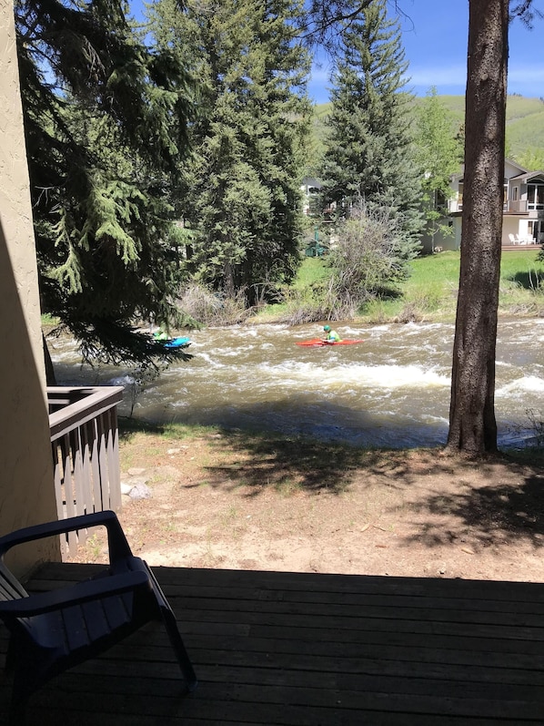 A river with a person kayaking, surrounded by trees and a building in the background.
