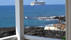 A cruise ship in the distance, rocky coastline, and outdoor seating area with chairs and an umbrella. - Platinum Partner Kona Priv Oceanfront 4 Bdrm  Pool Home Oct 14-20 Oct 29-Nov 7 (Kailua-Kona)