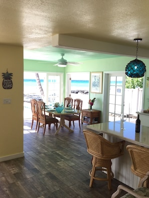 A dining area with a view of the ocean, wooden chairs, a table with glassware, and a ceiling fan.