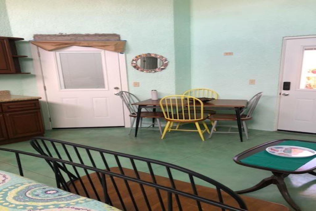 Un coin repas avec une table et des chaises, une porte avec un miroir, et un berceau au premier plan.