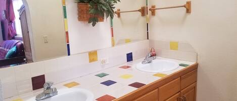 A bathroom with two sinks, wooden cabinets, a mirror, and a potted plant.