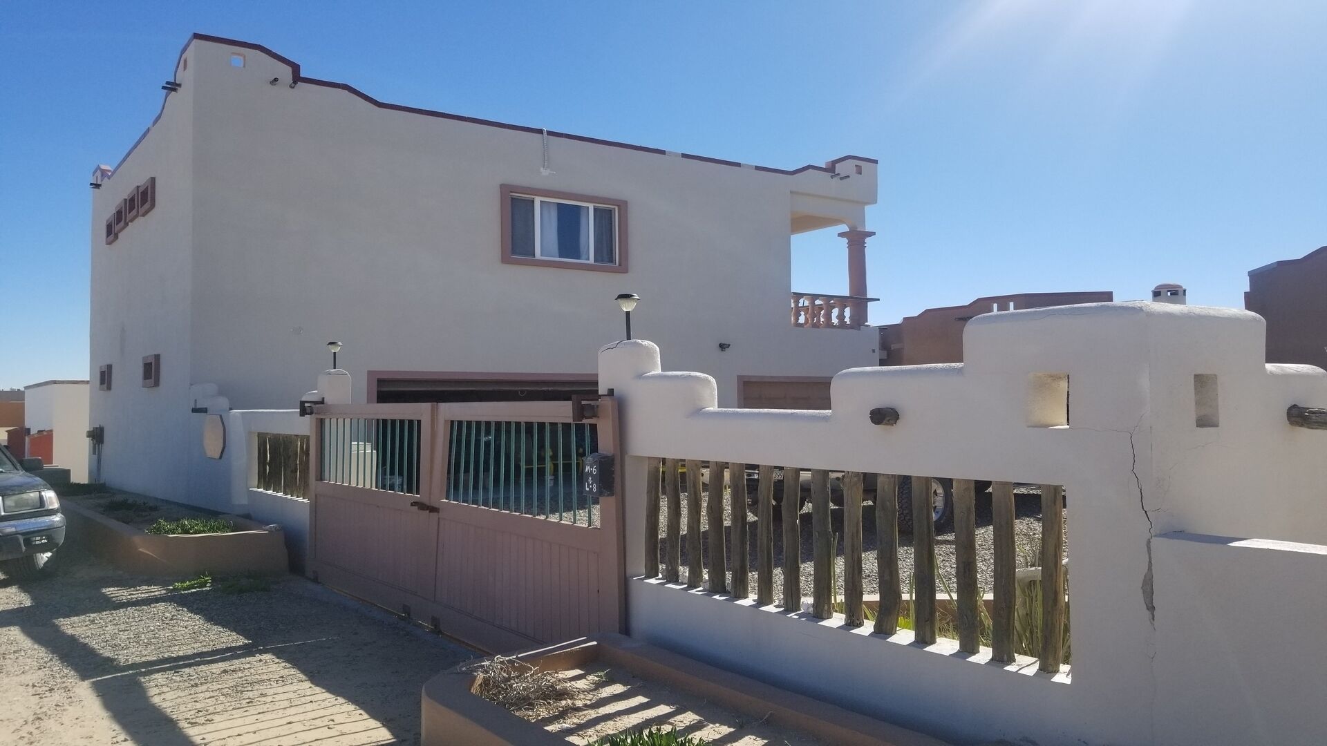 Un bâtiment blanc avec une entrée fermée par un portail, un petit balcon et une fenêtre.