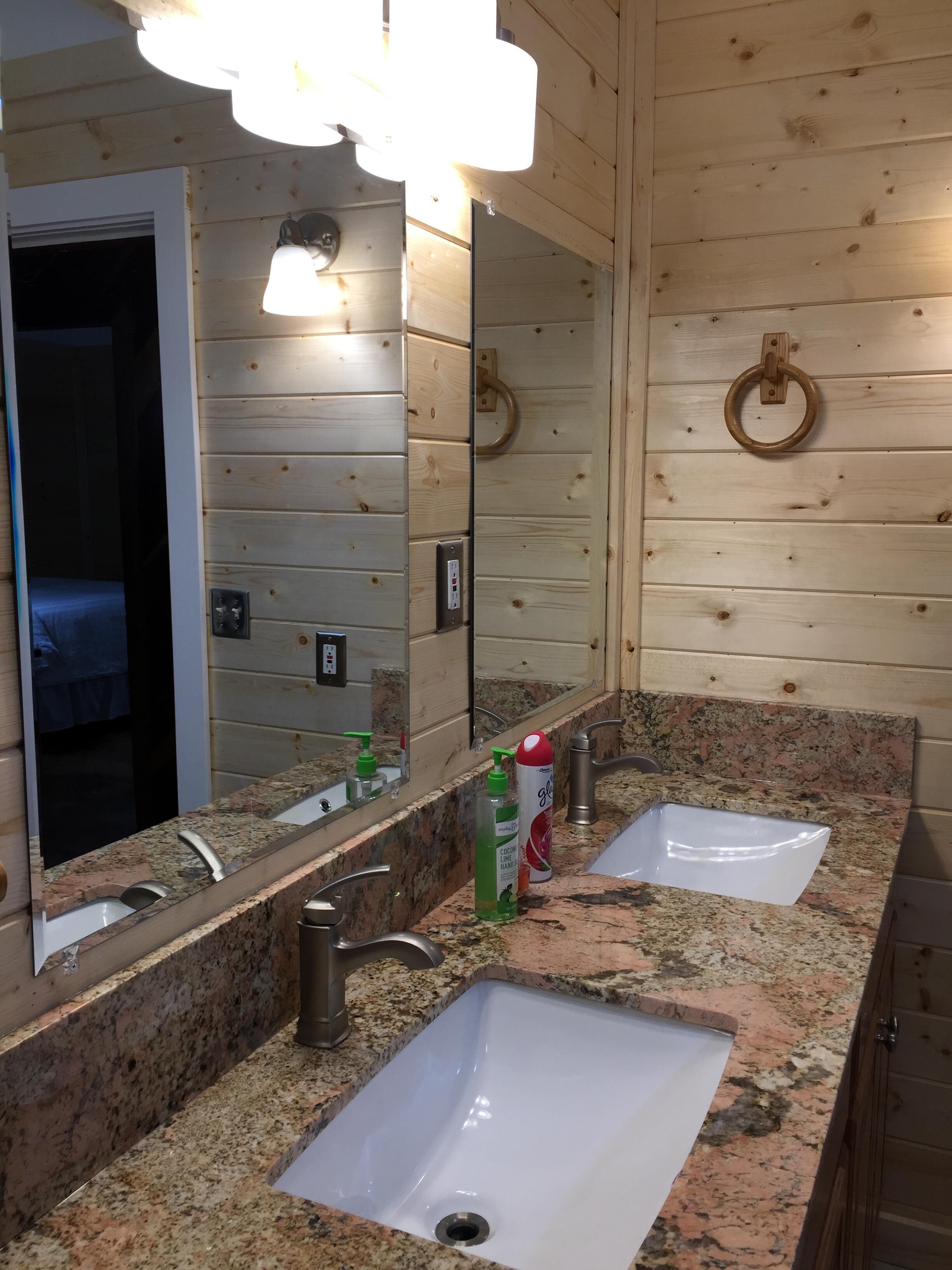 Un baño con dos lavamanos, un espejo grande, paredes de madera y una luz de aro.