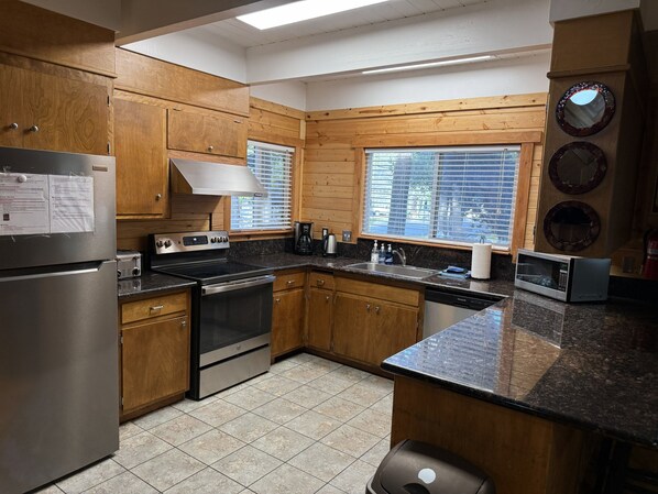 A kitchen with wooden cabinets, stainless steel appliances, a window with blinds, and a tiled floor.