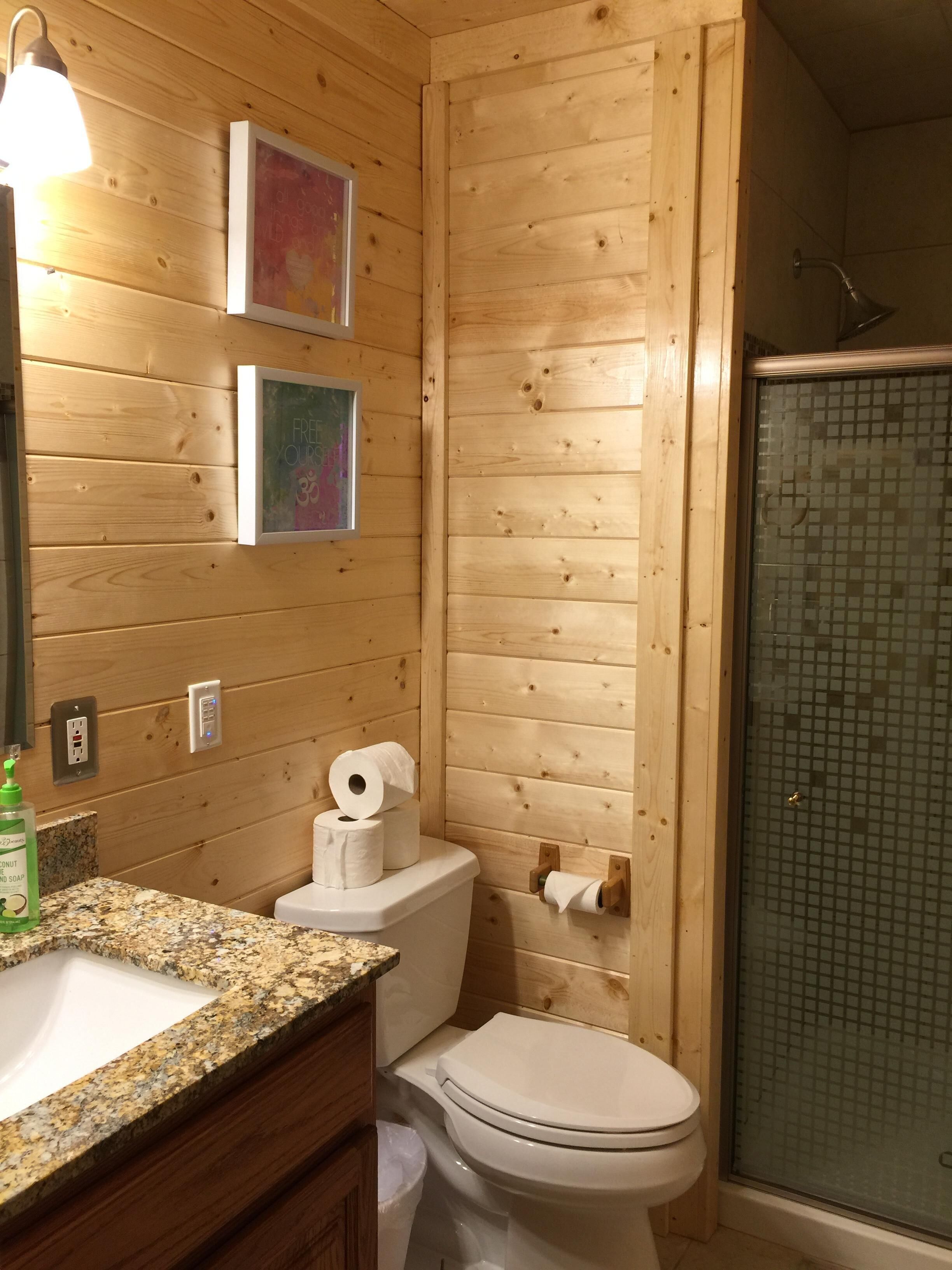 A wooden cabin bathroom with a granite countertop, a toilet, and a shower with a glass door.