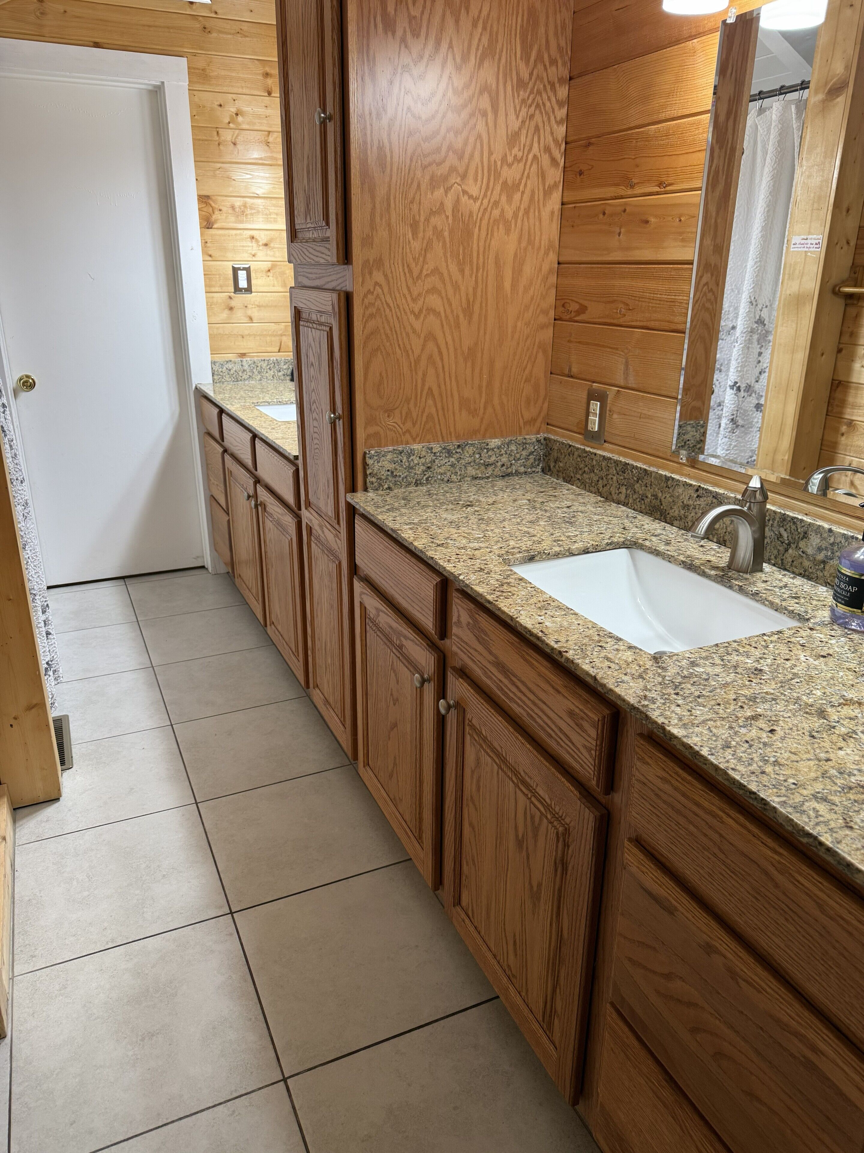 Un baño con paneles de madera, un lavamanos blanco, encimera de granito y un espejo sobre el lavamanos.