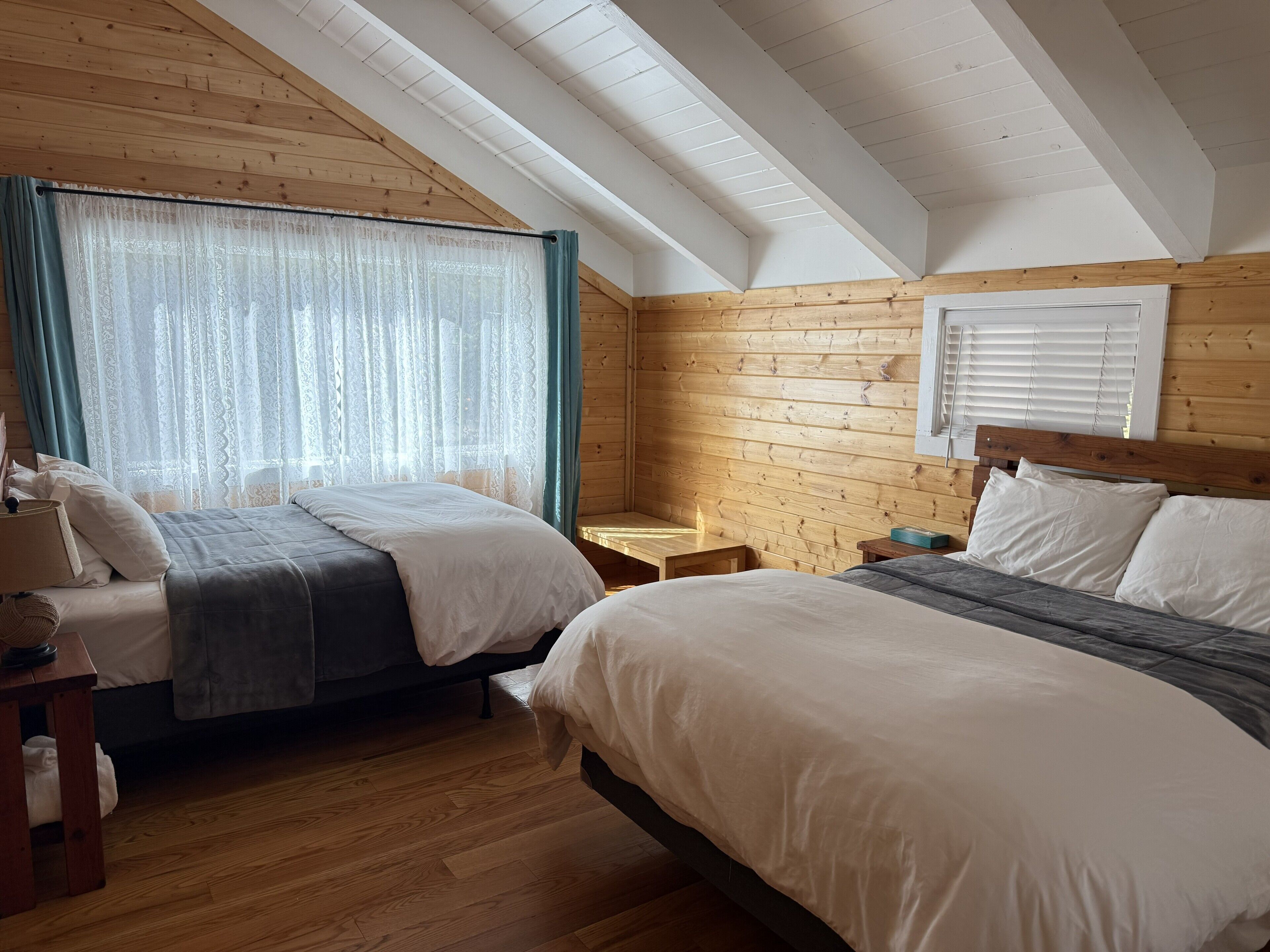 Ein gemütliches Zimmer mit zwei Betten, Holzwänden, einer schrägen Decke und einem Fenster mit Vorhängen.