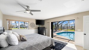 Une chambre avec un lit, un ventilateur de plafond, une télévision et une vue sur une piscine.