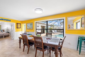 Un comedor con una mesa grande y sillas, vista a una piscina y una pared de color amarillo brillante.