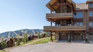A multi-story building with a stone facade, wooden balconies, and a driveway leading to a garage. - Deep Forest Retreat | Big Sky Ski-In/Out Luxury for 10 (Big Sky)