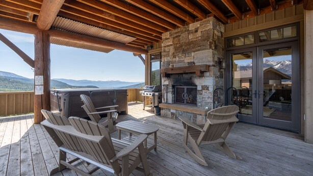 An outdoor deck with wooden chairs and a grill area, overlooking a mountainous landscape. - Deep Forest Retreat | Big Sky Ski-In/Out Luxury for 10 (Big Sky)