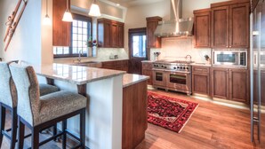 A modern kitchen with a central island, wooden cabinets, stainless steel appliances, and bar stools. - Deep Forest Retreat | Big Sky Ski-In/Out Luxury for 10 (Big Sky)