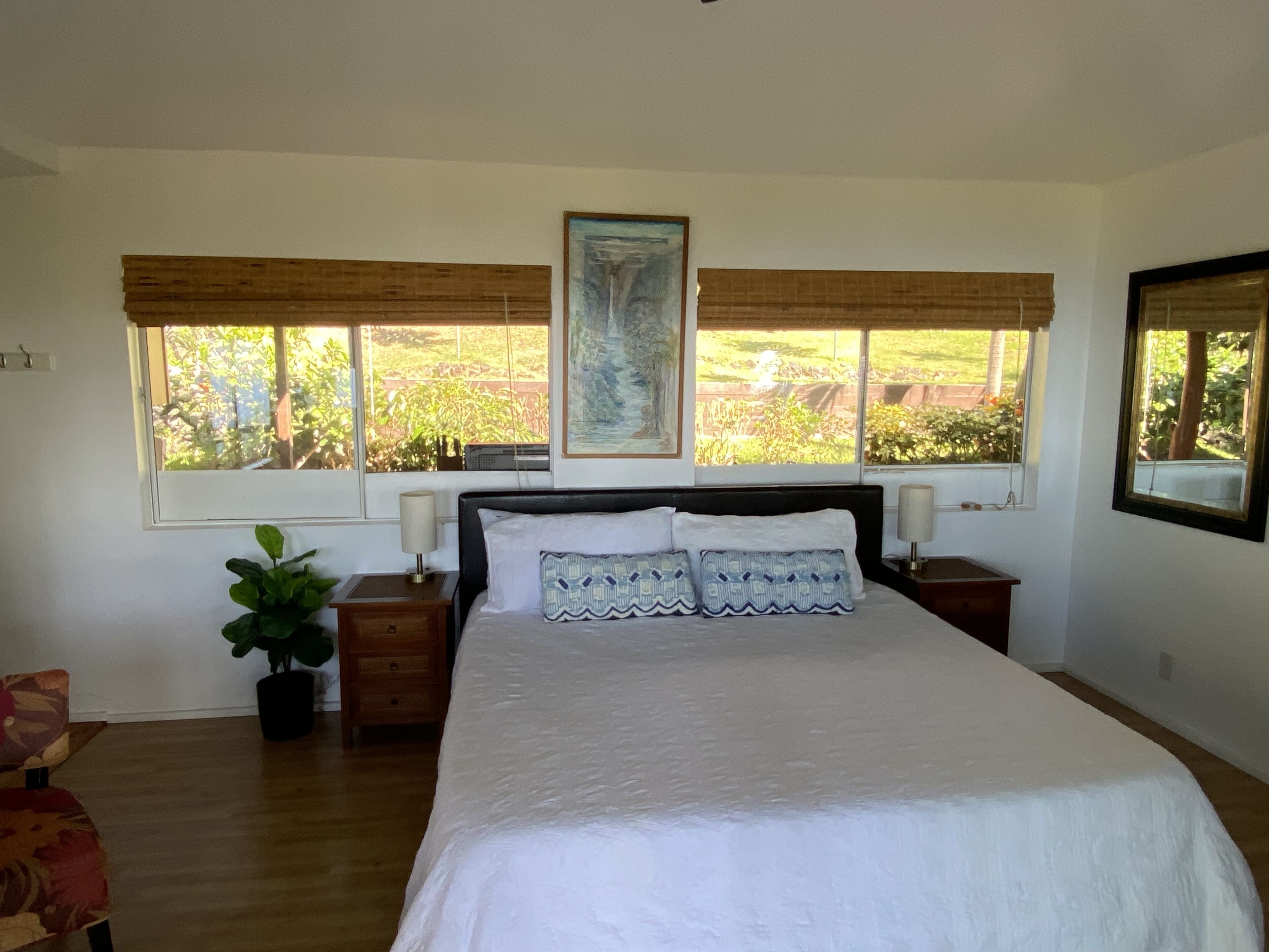 Un dormitorio con una cama grande, dos mesitas de noche, una planta en maceta y ventanas con persianas.