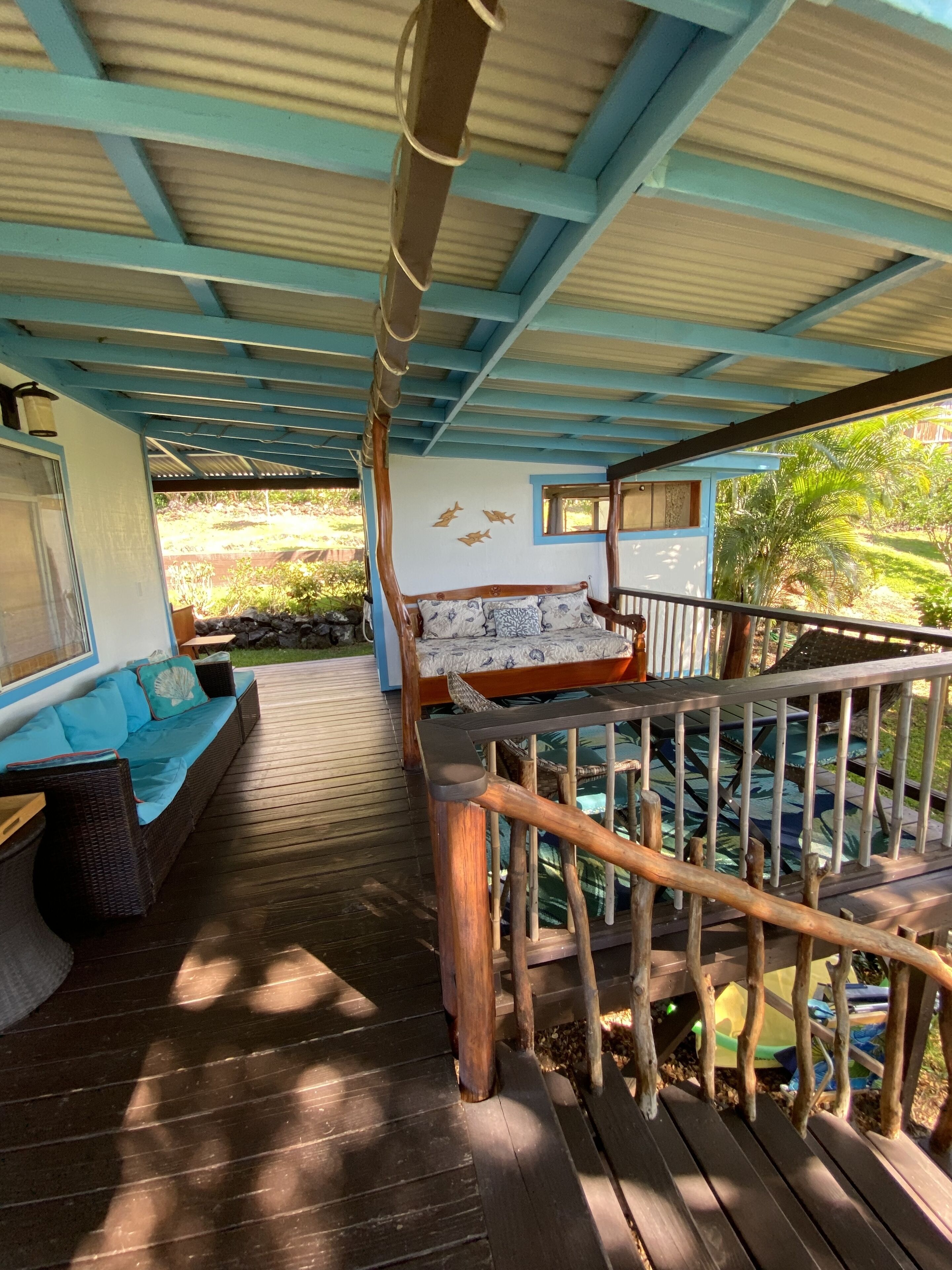 A covered outdoor deck with a wooden bench, a cushioned seating area, and a railing.