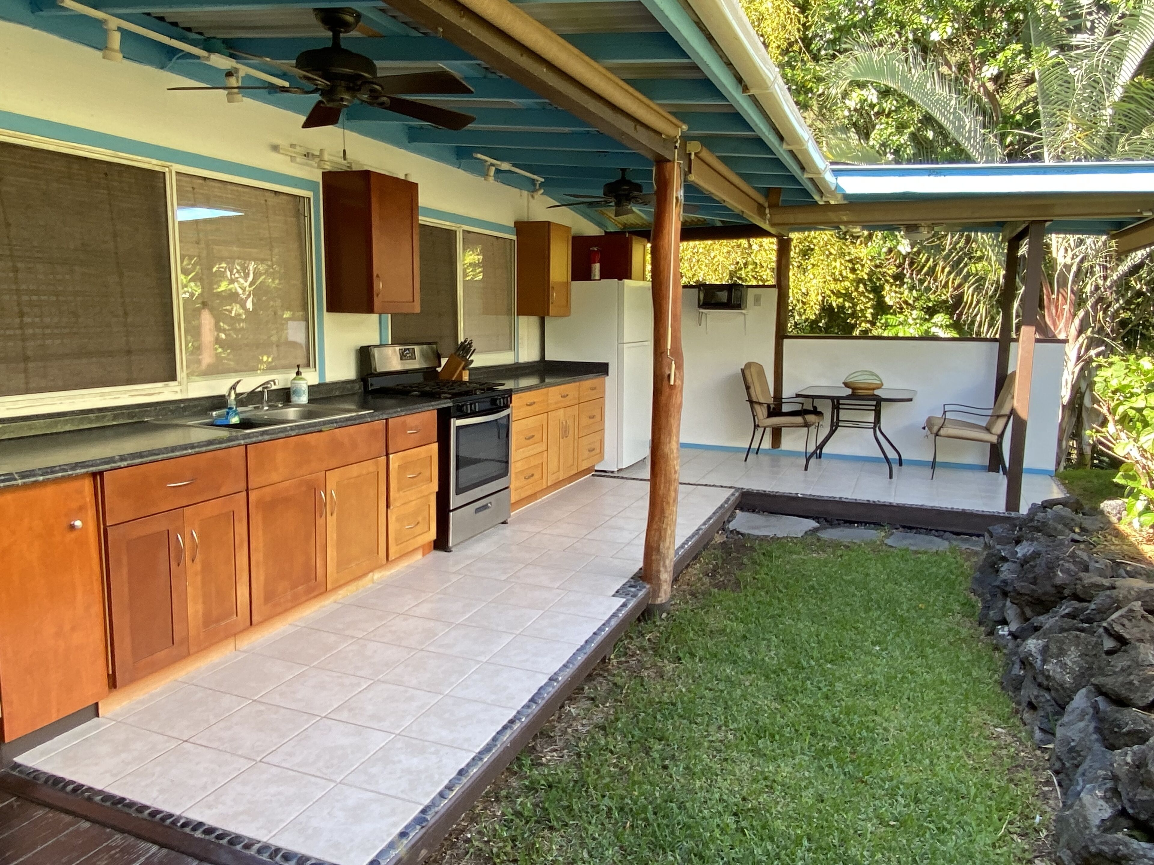 A kitchen with wooden cabinets, a gas stove, and a ceiling fan. There is a patio area with a table and chairs, and a small garden with a stone wall.