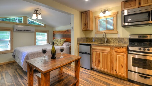 A compact kitchen with wooden cabinets, a built-in microwave, and a stainless steel oven. - Creekside Tiny Cabin w/ Hot Tub, Firepit, Pet Friendly, Near NOC, Tsali & Dragon (Almond)