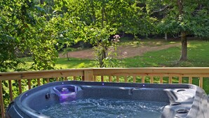 A hot tub on a wooden deck with a view of a grassy yard and trees. - Creekside Tiny Cabin w/ Hot Tub, Firepit, Pet Friendly, Near NOC, Tsali & Dragon (Almond)
