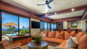 A spacious living area with a large sofa, wicker chairs, a round coffee table, and a view of the ocean. - Mauna Kea Villa, Walking Distance to the Beach and Hotel - Beyond Perfection! (Kamuela)