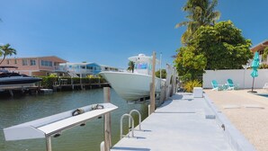Un port de plaisance avec des bateaux amarrés, un espace piscine avec des chaises longues et un bâtiment doté de balcons.