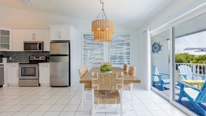 Une cuisine moderne dotée d’appareils électroménagers en acier inoxydable, un coin repas avec une table en bois et des chaises en osier, et une grande fenêtre offrant une vue sur l’extérieur.