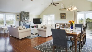 A spacious living room with a fireplace, two sofas, a dining table with chairs, and ceiling fans. - Beautiful home with private heated pool, basketball and large outdoor space. (Nantucket)