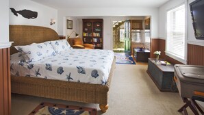 A bedroom with a large bed, a bookshelf, a wicker chair, and a desk with a vase of flowers. - Beautiful home with private heated pool, basketball and large outdoor space. (Nantucket)