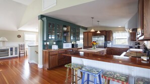A spacious kitchen with wooden cabinets, a central island, and bar stools. - Beautiful home with private heated pool, basketball and large outdoor space. (Nantucket)