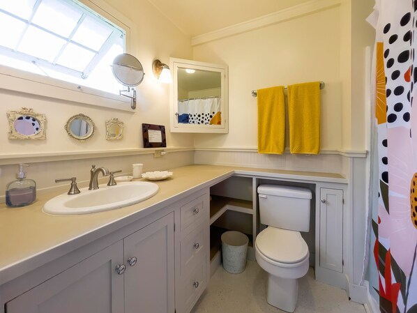 A bathroom with a sink, mirror, toilet, and a window.