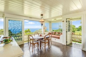 Enjoy ocean views from the large windows in this room, which features a dining table, bench, and hanging light fixture.