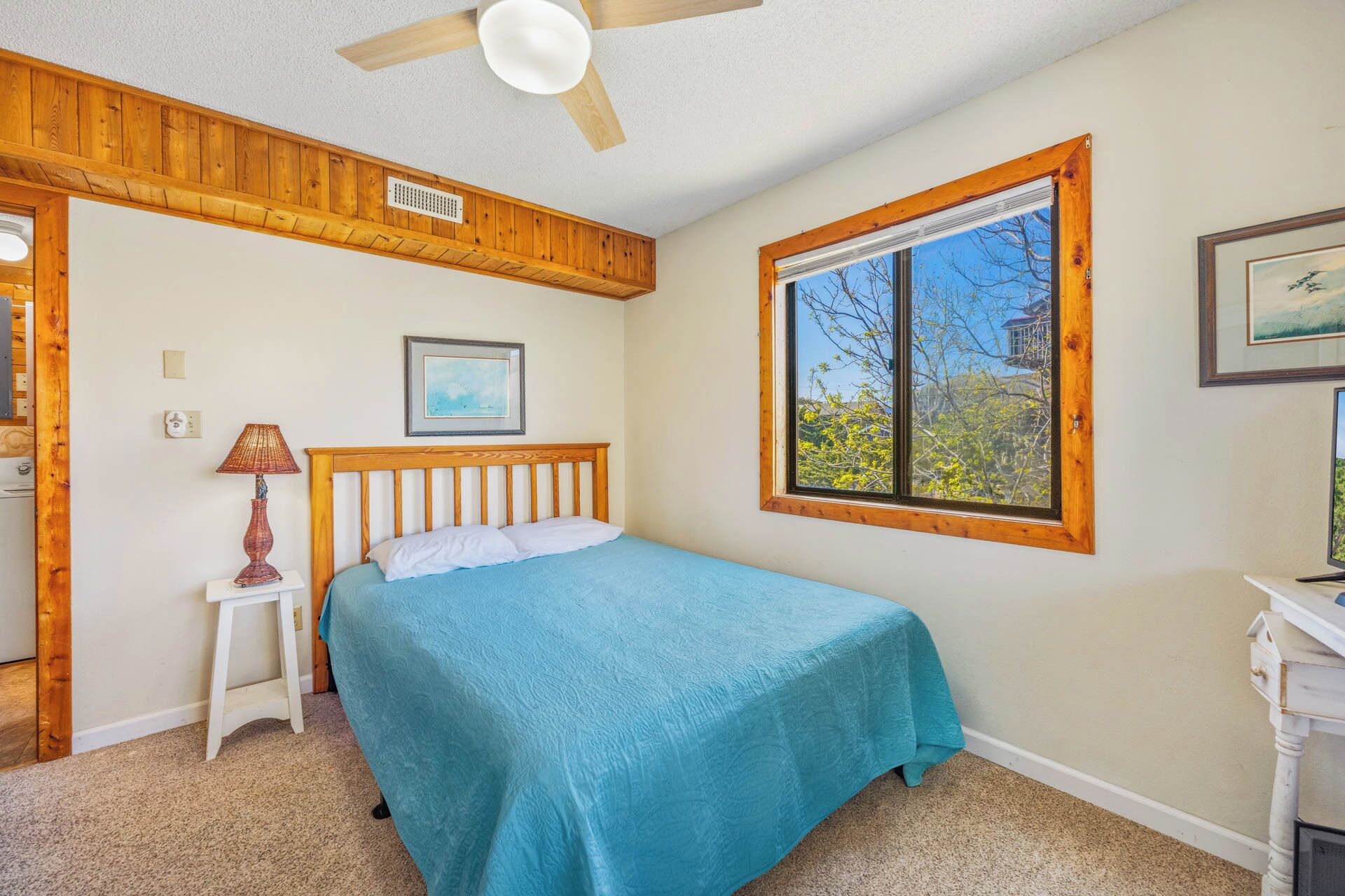 A bedroom with a bed, a window, a ceiling fan, and a framed picture on the wall.