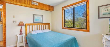 A bedroom with a bed, a window, a ceiling fan, and a framed picture on the wall.