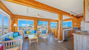 A spacious living area with a sofa, chairs, and a dining table. There is a kitchen area with a sink and a microwave. The room has large windows and a view of the outside. - Oceanview Dog Friendly w/ Hot Tub, Games, Community Pool and Tennis/Pickleball (Avon)
