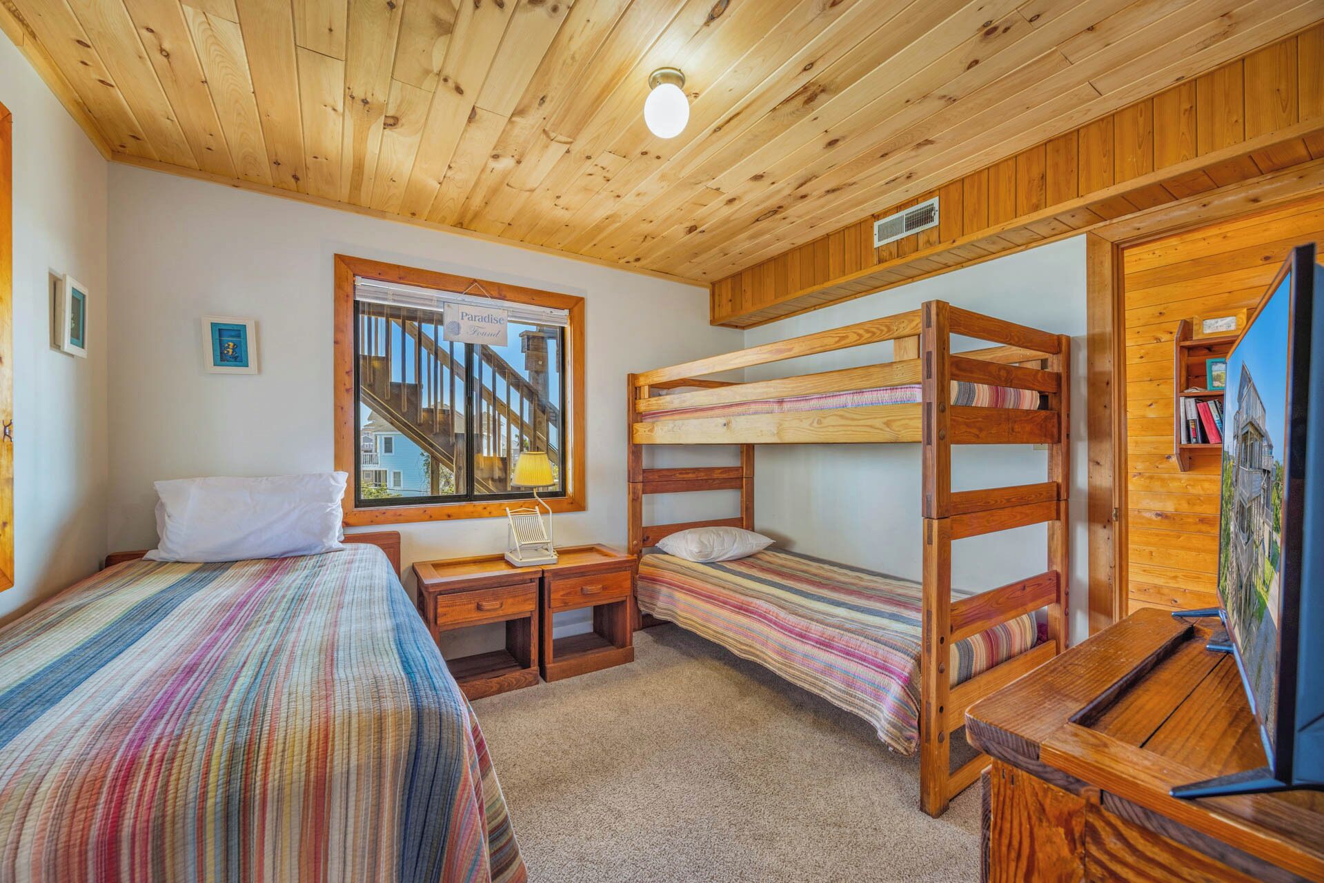 A room with bunk beds, a desk, a chair, a lamp, and a window with a view of a staircase.