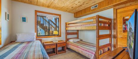 A room with bunk beds, a desk, a chair, a lamp, and a window with a view of a staircase.