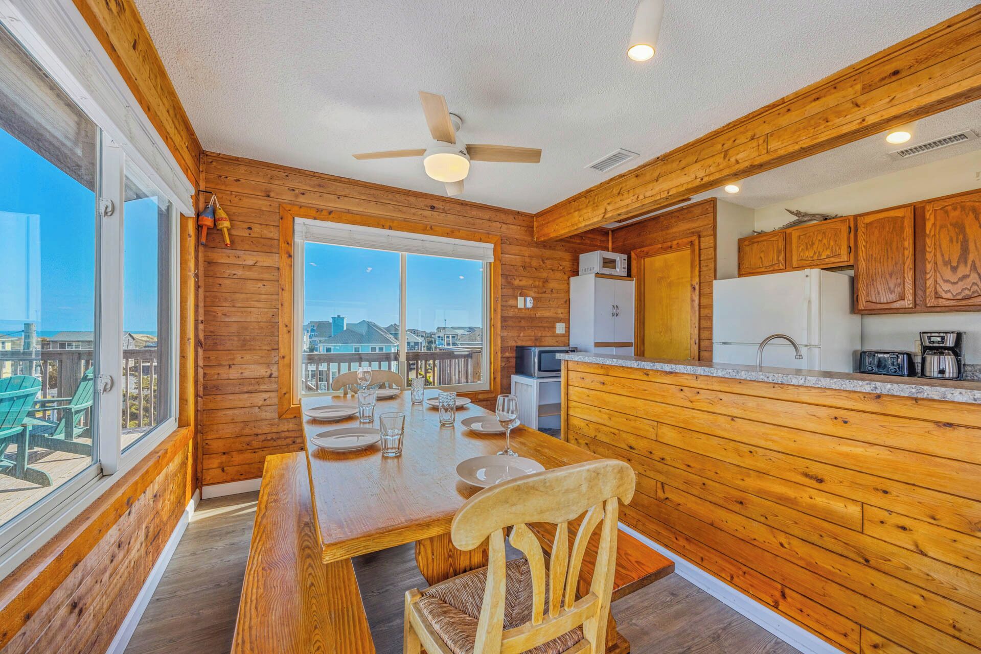 Un intérieur en bois avec une table à manger pour deux personnes, une cuisine dotée de meubles en bois et une vue dégagée sur l’extérieur grâce à une grande fenêtre.