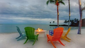 Une plage avec des chaises colorées, un petit foyer et des palmiers.